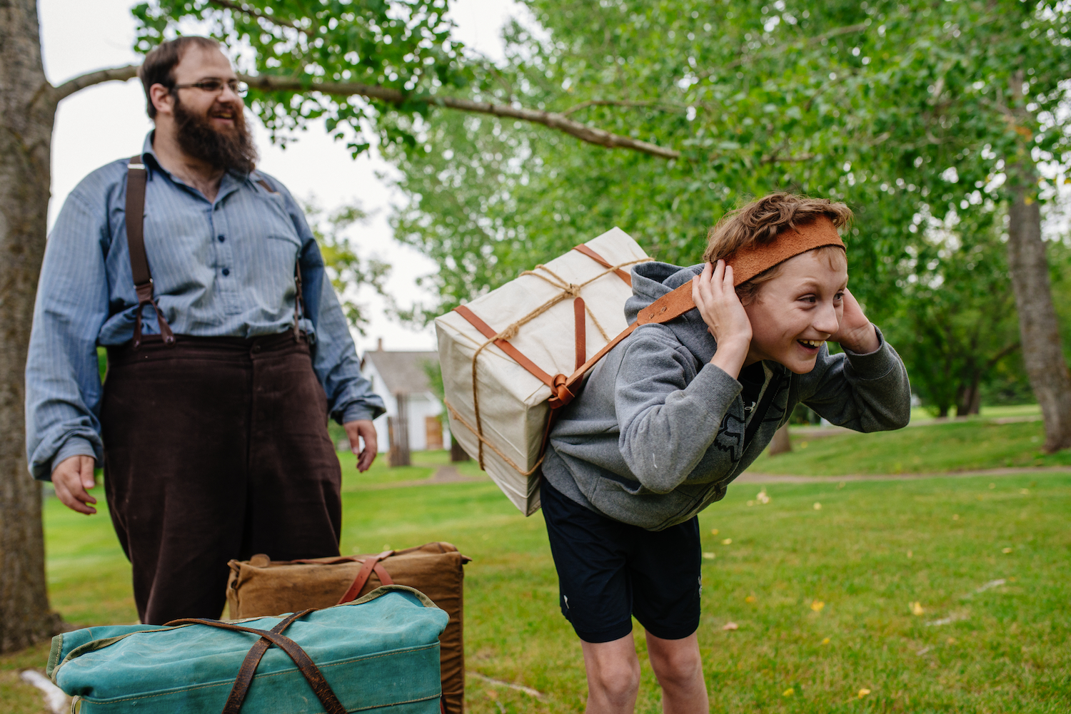 A visitor tries carrying a bale with a tumpline as a historical interpreter looks on